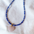 Necklace with blue beads and a pink heart pendant on a white fabric background
