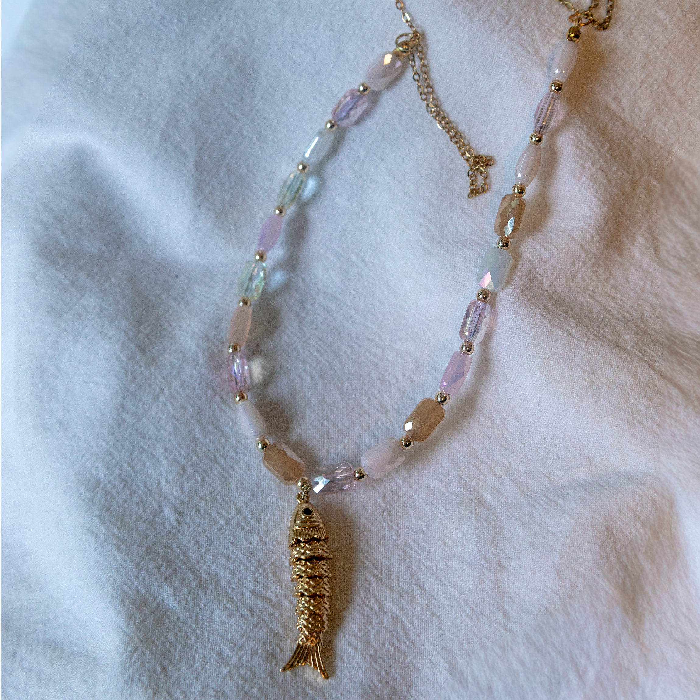 Necklace with a gold fish pendant on a white fabric background